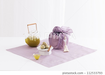 There are kettles, teacups and rice cakes around the gift wrapped in cloth 112533793