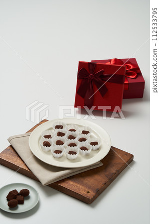 There is a plate of handmade chocolate in a cup of parchment paper and a gift box next to it There is a plate of handmade chocolate in a cup of parchment paper and a gift box next to it 112533795
