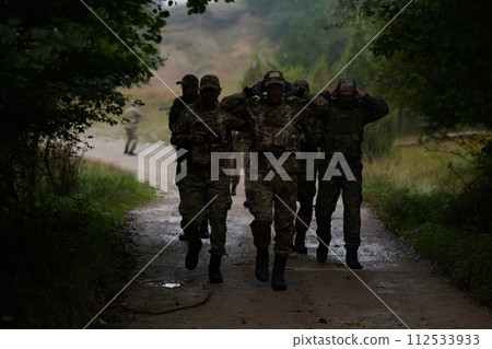 A group of elite soldiers leads captives through a military camp, showcasing a tense atmosphere of detention and security operations 112533933