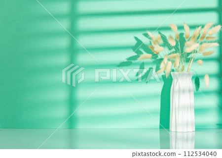 Vase with dry flowers against mint background with shadow pattern Vase with dry flowers against mint background with shadow pattern 112534040