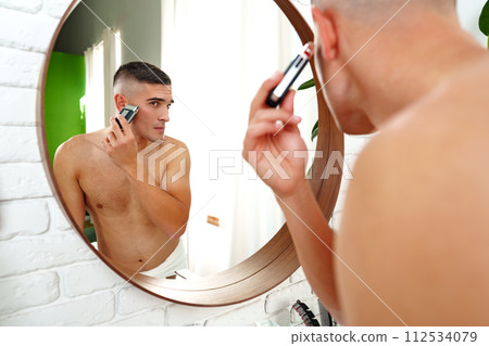 Handsome young man shaving face with electric razor on white background 112534079