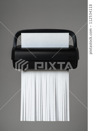 Black paper shredder cutting paper on gray background Black paper shredder cutting paper on gray background 112534118