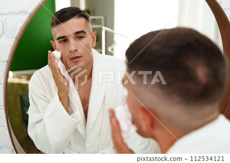 Reflection of a young man shaving in bathroom mirror close up Reflection of a young man shaving in bathroom mirror close up 112534121