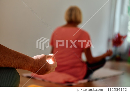 In this sunlit space, a senior woman's hand gracefully engages in various yoga poses, embodying the essence of active aging, health, and inner peace In this sunlit space, a senior woman's hand gracefully engages in various yoga poses, embodying the essence of active aging, health, and inner peace 112534152