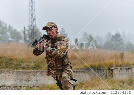 An elite soldier, camouflaged and stealthily navigating through dangerous woodland terrain, executes a covert mission in a secluded forest area 112534198