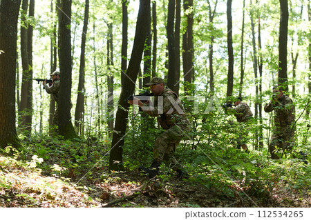 A specialized military antiterrorist unit conducts a covert operation in dense, hazardous woodland, demonstrating precision, discipline, and strategic readiness 112534265