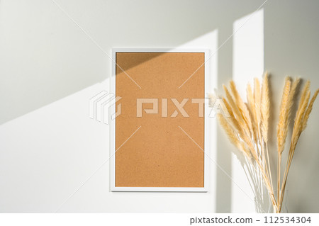White blank photo frame with dry flowers in vase against white wall 112534304