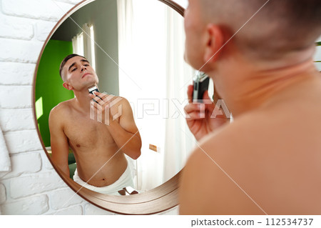 Handsome young man shaving face with electric razor on white background Handsome young man shaving face with electric razor on white background 112534737
