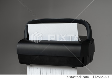 Black paper shredder cutting paper on gray background 112535024