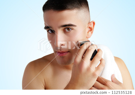 Handsome young man shaving face with electric razor on white background 112535128