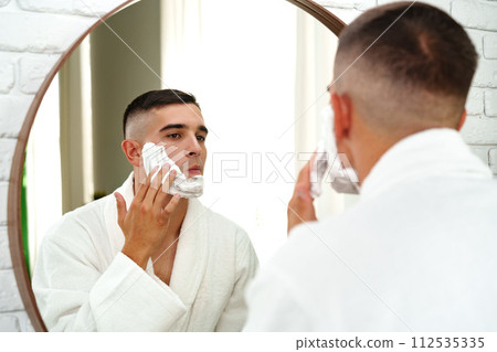Reflection of a young man shaving in bathroom mirror close up 112535335