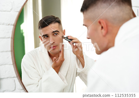 Reflection of a young man shaving in bathroom mirror close up Reflection of a young man shaving in bathroom mirror close up 112535355