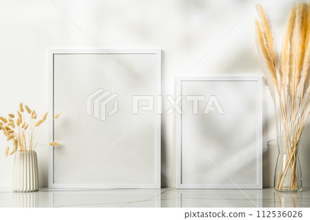 White blank photo frame with dry flowers in vase against white wall White blank photo frame with dry flowers in vase against white wall 112536026