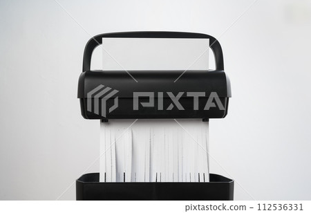 Black paper shredder cutting paper on gray background Black paper shredder cutting paper on gray background 112536331
