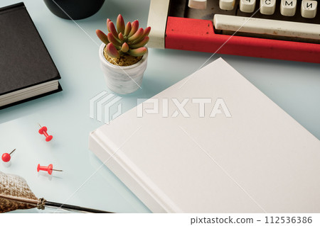 Hardcover book and vintage typewriter on white desk 112536386