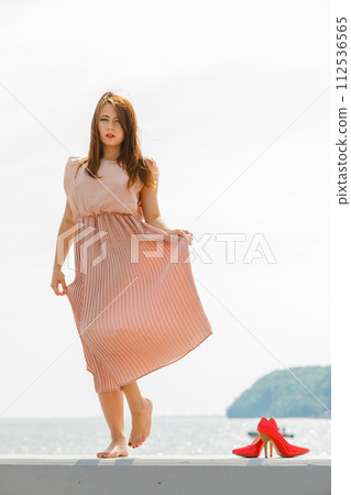 Woman wearing long light pink dress on jetty Woman wearing long light pink dress on jetty 112536565
