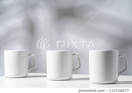 White ceramic mugs on gray background with shadows White ceramic mugs on gray background with shadows 112536677