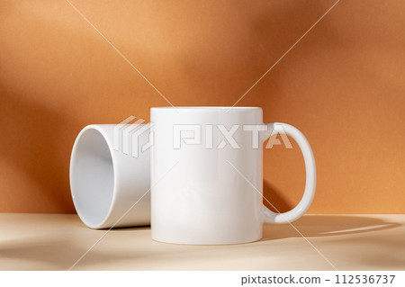 White ceramic mugs on peach background with shadows 112536737
