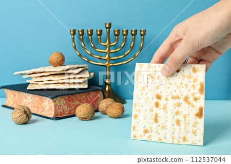 Matzo in hand, Torah, Hanukkiah and nuts on blue background 112537044