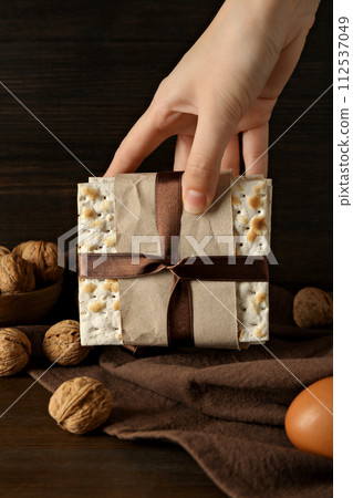 Matzo in hand, nuts and egg on wooden background Matzo in hand, nuts and egg on wooden background 112537049