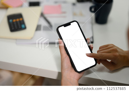 Closeup of businesswoman holding smartphone with empty screen sitting at office desk Closeup of businesswoman holding smartphone with empty screen sitting at office desk 112537885