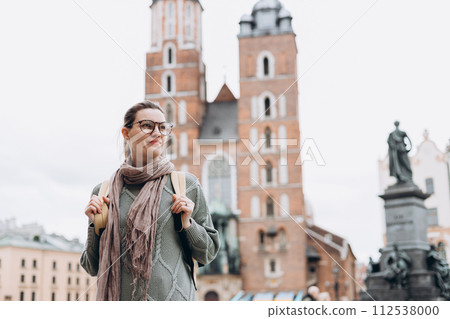 Tourist happy woman in glasses on Market Square in Krakow, Traveling Europe in autumn. St. Marys Basilica, cloudy day Tourist happy woman in glasses on Market Square in Krakow, Traveling Europe in autumn. St. Marys Basilica, cloudy day 112538000
