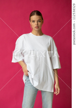 Beautiful blonde girl in a white oversized T-shirt and blue jeans posing on a gray background Beautiful blonde girl in a white oversized T-shirt and blue jeans posing on a gray background 112538329