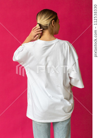 Beautiful blonde girl in a white oversized T-shirt and blue jeans posing on a gray background 112538330