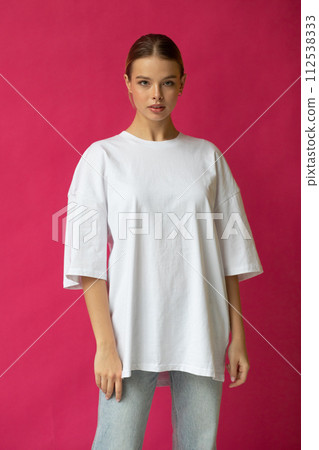 Beautiful blonde girl in a white oversized T-shirt and blue jeans posing on a gray background 112538333