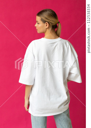 Beautiful blonde girl in a white oversized T-shirt and blue jeans posing on a gray background Beautiful blonde girl in a white oversized T-shirt and blue jeans posing on a gray background 112538334