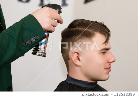 Moistening with water from a spray bottle before cutting with scissors. Caucasian bearded man having his hair sprayed by a barber. 112538399