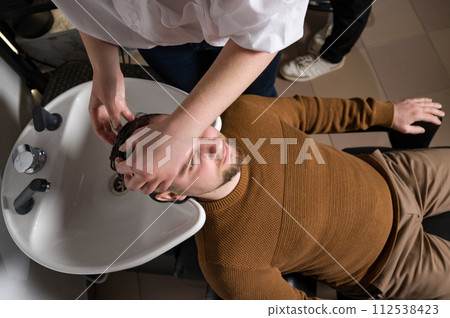Barber shampooing washing a male clients head in the sink. Barber shampooing washing a male clients head in the sink. 112538423