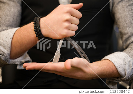 Closeup of a barber holding a dangerous razor in the shape of a triangle. 112538442