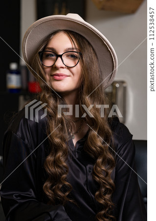 Portrait of a young girl in a hat and with long hair. A female student is sitting in the classroom during a break between pairs. Portrait of a young girl in a hat and with long hair. A female student is sitting in the classroom during a break between pairs. 112538457