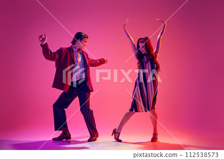 Young man and woman in stylish clothes dancing retro dance, boogie woogie against pink background in neon light Young man and woman in stylish clothes dancing retro dance, boogie woogie against pink background in neon light 112538573