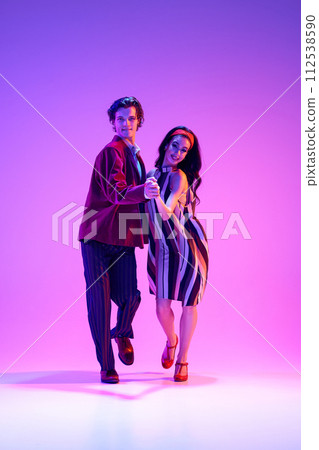 Artistic, talented, positive young man and woman, stylish couple dancing retro dance, boogie woogie against purple background in neon light 112538590