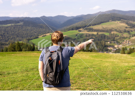 Men pointing finger on mountains background. Young male with backpack hiking in nature. Back view. Travel and active lifestyle concept. 112538636