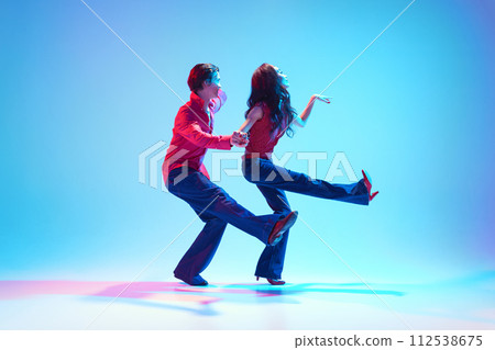 Rockability era. Retro dance aesthetics. Young stylish man and woman dancing against blue background in neon light 112538675