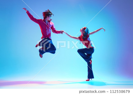 Stylish handsome young man and beautiful woman dancing rock and roll retro dance against blue background in neon light Stylish handsome young man and beautiful woman dancing rock and roll retro dance against blue background in neon light 112538679