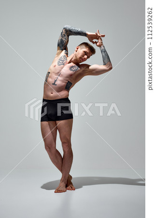 Young man with muscular, athletic body posing in underwear raising arms against grey studio background. Copy space. 112539262