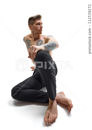 Tattooed, handsome, shitless young man posing sitting on floor against white studio background. Copy space. Tattooed, handsome, shitless young man posing sitting on floor against white studio background. Copy space. 112539272