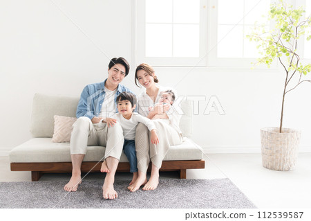 A close Asian (Japanese) family of four looking at the camera in a newly built room under bright sunlight. Wide angle 112539587