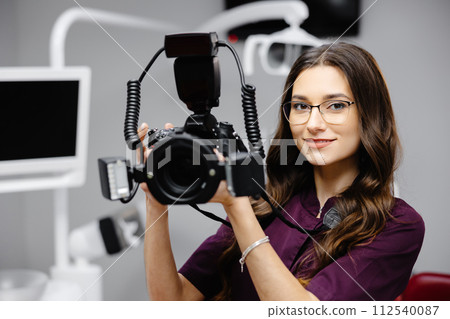Portrait of female dentist holding photo camera in hands, standing in dental office 112540087