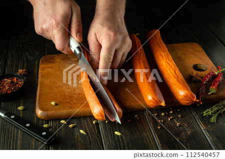 Chef hands using a knife to cut Munich smoked sausages before preparing dinner on the kitchen table. Meat dish cooking concept 112540457