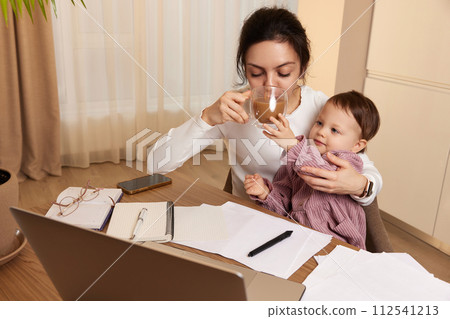 beautiful businesswoman working at home with her little child girl and drinking coffee 112541213