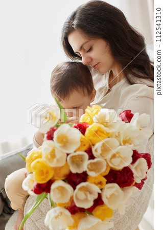 Cute little baby daughter and mom with flowers tulips. Mother and child hugging. Happy mother's day. 112541310