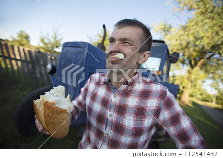 The village man tractor driver is hungry and is eating a loaf. 112541432