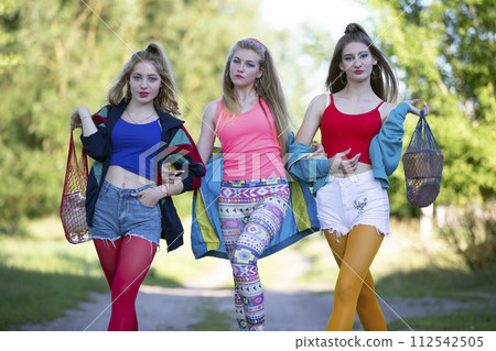 Three beautiful country girls dressed in the style of the nineties are walking along the road. Three beautiful country girls dressed in the style of the nineties are walking along the road. 112542505