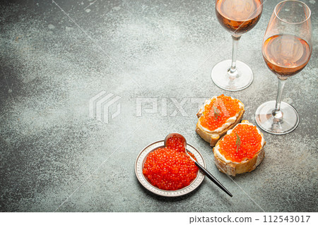 Small metal plate with red salmon caviar, two caviar toasts canape, two glasses of champagne top view on grey concrete background, festive luxury delicacy and appetizer. Space for text 112543017