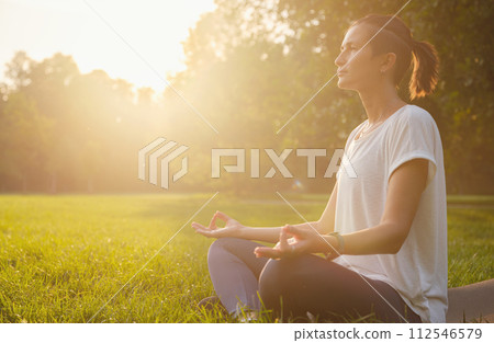 Young asian woman doing meditation in morning or evening at park, healthy woman relaxing and practicing yoga at city park. Mindfulness, destress, Healthy habits and balance concept 112546579